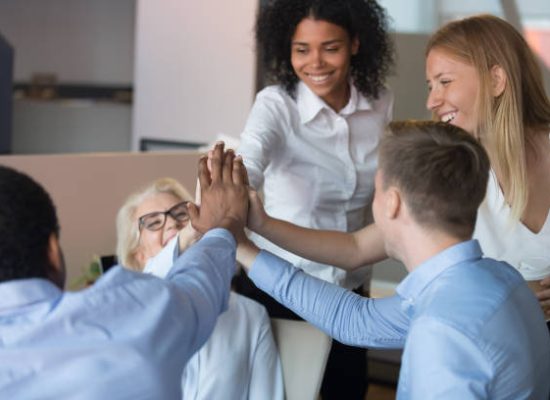 Happy multi-ethnic employees accomplish working on project celebrating unbelievable success giving high five stacking their palms hands together. Rewarding advancement, team spirit and support concept